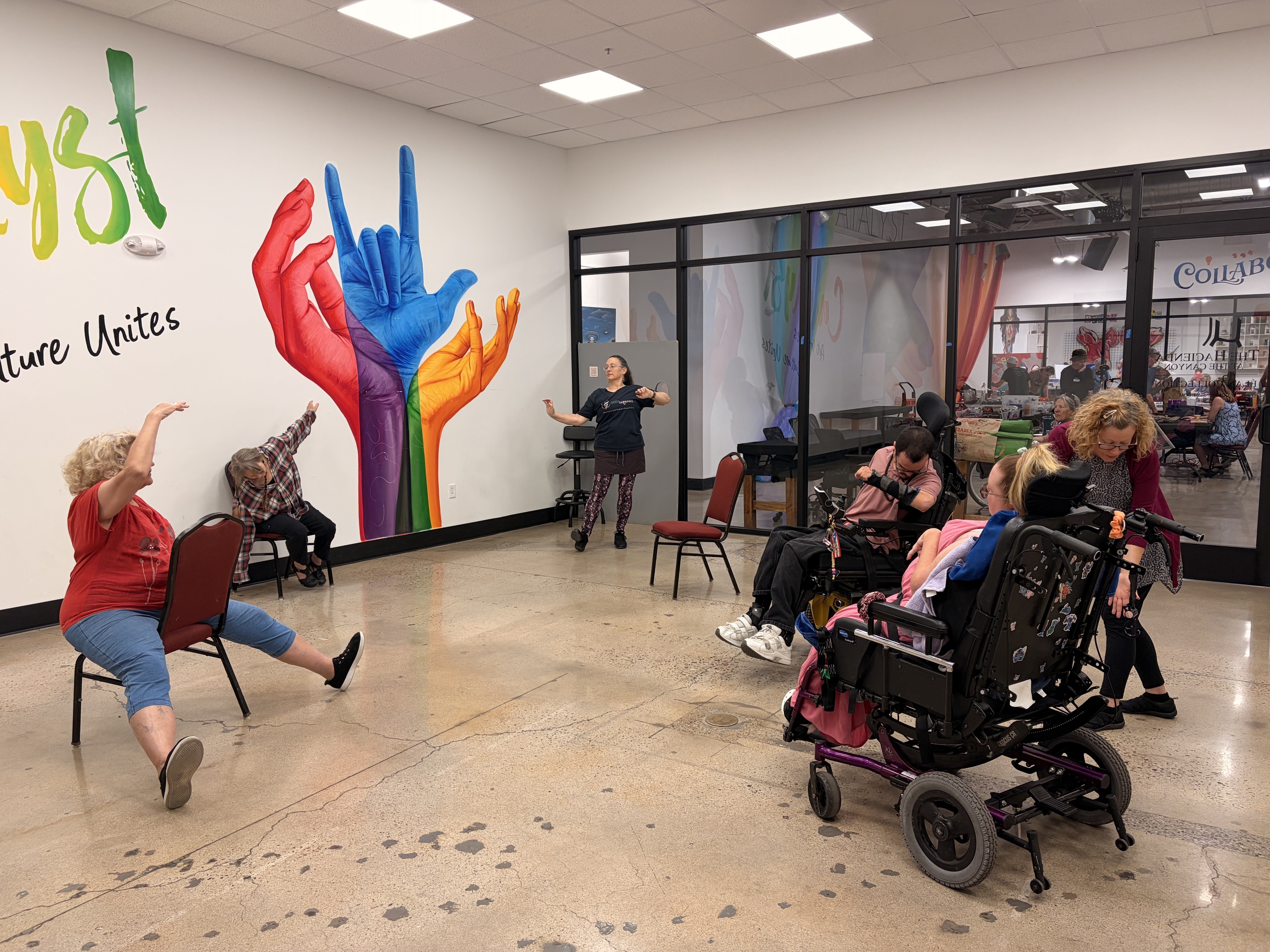 Participants moving together in chairs and wheelchairs during a Community Open Sharing session at the Catalyst